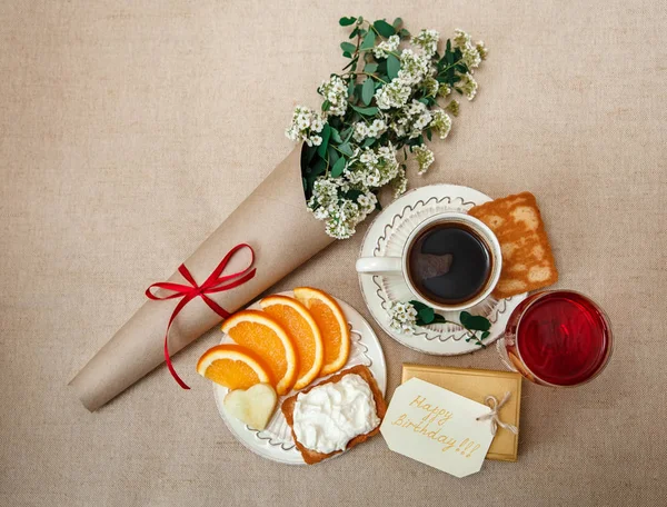 Romantic Birthday Healthy Breakfast.Cup of Coffee,Cut Orange,Biscuit with Cottage Cheese.Glass of red Beverage.Wish Card with Flowers.Present in Golden Box