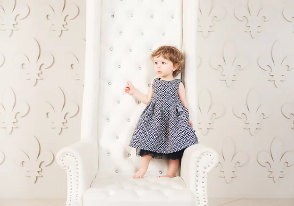 Linda niña pequeña en hermoso vestido en silla . — Foto de Stock