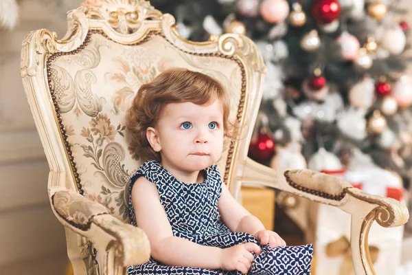 Linda niña pequeña con la cara divertida está sentado en el árbol de background.Christmas árbol background.Studio árbol de Navidad shooting.Holiday concepto — Foto de Stock