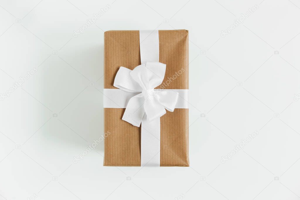 Gift box wrapped in craft paper with white ribbon. Present box on the white background. Holiday present. Top view.Vertical