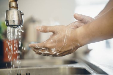 Koronavirüsün yayılmasını önlemek için her zaman temiz ellerle başlayın (Covid-19). Asyalı bir adamın evde ellerini yıkarken çekilmiş görüntüsü.