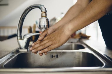 Koronavirüsün yayılmasını önlemek için her zaman temiz ellerle başlayın (Covid-19). Asyalı bir adamın evde ellerini yıkarken çekilmiş görüntüsü.