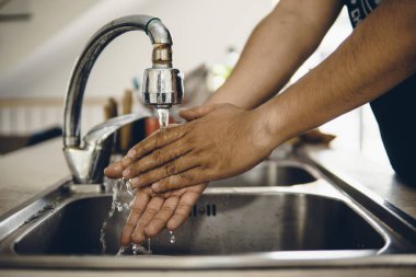 Koronavirüsün yayılmasını önlemek için her zaman temiz ellerle başlayın (Covid-19). Asyalı bir adamın evde ellerini yıkarken çekilmiş görüntüsü.