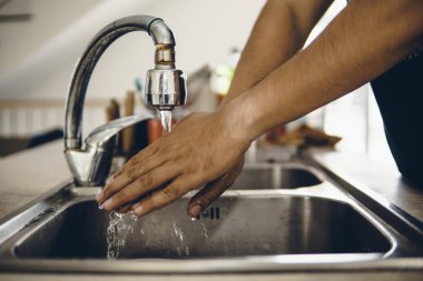 Koronavirüsün yayılmasını önlemek için her zaman temiz ellerle başlayın (Covid-19). Asyalı bir adamın evde ellerini yıkarken çekilmiş görüntüsü.