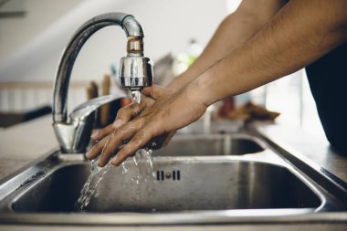 Koronavirüsün yayılmasını önlemek için her zaman temiz ellerle başlayın (Covid-19). Asyalı bir adamın evde ellerini yıkarken çekilmiş görüntüsü.