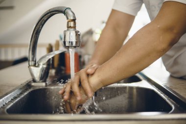 Koronavirüsün yayılmasını önlemek için her zaman temiz ellerle başlayın (Covid-19). Asyalı bir adamın evde ellerini yıkarken çekilmiş görüntüsü.