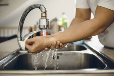 Koronavirüsün yayılmasını önlemek için her zaman temiz ellerle başlayın (Covid-19). Asyalı bir adamın evde ellerini yıkarken çekilmiş görüntüsü.