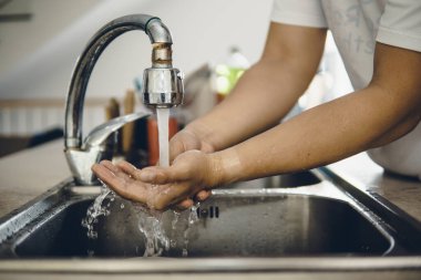 Koronavirüsün yayılmasını önlemek için her zaman temiz ellerle başlayın (Covid-19). Asyalı bir adamın evde ellerini yıkarken çekilmiş görüntüsü.