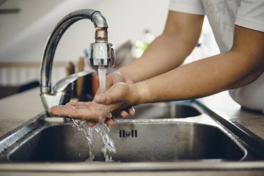 Koronavirüsün yayılmasını önlemek için her zaman temiz ellerle başlayın (Covid-19). Asyalı bir adamın evde ellerini yıkarken çekilmiş görüntüsü.