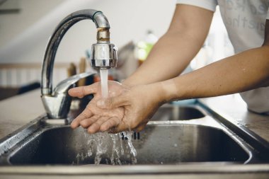 Koronavirüsün yayılmasını önlemek için her zaman temiz ellerle başlayın (Covid-19). Asyalı bir adamın evde ellerini yıkarken çekilmiş görüntüsü.