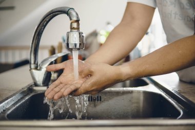 Koronavirüsün yayılmasını önlemek için her zaman temiz ellerle başlayın (Covid-19). Asyalı bir adamın evde ellerini yıkarken çekilmiş görüntüsü.