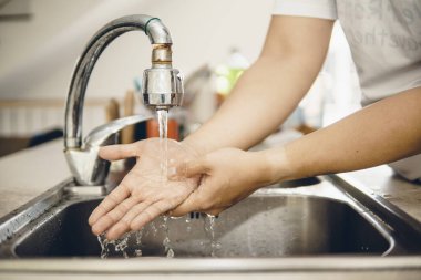 Koronavirüsün yayılmasını önlemek için her zaman temiz ellerle başlayın (Covid-19). Asyalı bir adamın evde ellerini yıkarken çekilmiş görüntüsü.