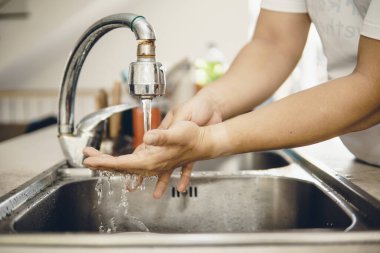 Koronavirüsün yayılmasını önlemek için her zaman temiz ellerle başlayın (Covid-19). Asyalı bir adamın evde ellerini yıkarken çekilmiş görüntüsü.