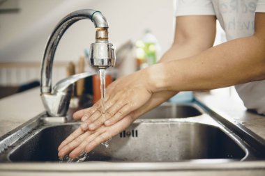 Koronavirüsün yayılmasını önlemek için her zaman temiz ellerle başlayın (Covid-19). Asyalı bir adamın evde ellerini yıkarken çekilmiş görüntüsü.