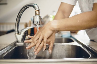 Koronavirüsün yayılmasını önlemek için her zaman temiz ellerle başlayın (Covid-19). Asyalı bir adamın evde ellerini yıkarken çekilmiş görüntüsü.