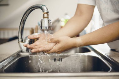 Koronavirüsün yayılmasını önlemek için her zaman temiz ellerle başlayın (Covid-19). Asyalı bir adamın evde ellerini yıkarken çekilmiş görüntüsü.