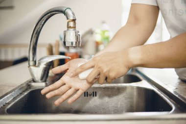 Koronavirüsün yayılmasını önlemek için her zaman temiz ellerle başlayın (Covid-19). Asyalı bir adamın evde ellerini yıkarken çekilmiş görüntüsü.