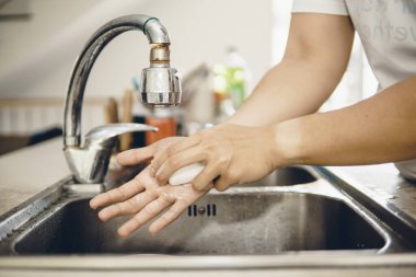 Koronavirüsün yayılmasını önlemek için her zaman temiz ellerle başlayın (Covid-19). Asyalı bir adamın evde ellerini yıkarken çekilmiş görüntüsü.