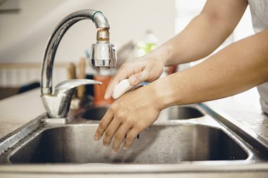 Koronavirüsün yayılmasını önlemek için her zaman temiz ellerle başlayın (Covid-19). Asyalı bir adamın evde ellerini yıkarken çekilmiş görüntüsü.