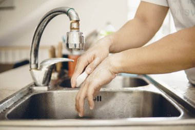 Koronavirüsün yayılmasını önlemek için her zaman temiz ellerle başlayın (Covid-19). Asyalı bir adamın evde ellerini yıkarken çekilmiş görüntüsü.