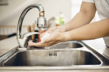 Koronavirüsün yayılmasını önlemek için her zaman temiz ellerle başlayın (Covid-19). Asyalı bir adamın evde ellerini yıkarken çekilmiş görüntüsü.