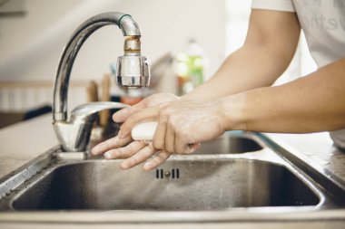 Koronavirüsün yayılmasını önlemek için her zaman temiz ellerle başlayın (Covid-19). Asyalı bir adamın evde ellerini yıkarken çekilmiş görüntüsü.