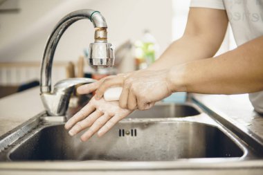 Koronavirüsün yayılmasını önlemek için her zaman temiz ellerle başlayın (Covid-19). Asyalı bir adamın evde ellerini yıkarken çekilmiş görüntüsü.