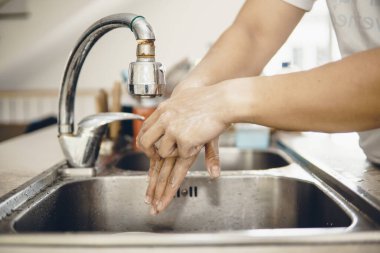 Koronavirüsün yayılmasını önlemek için her zaman temiz ellerle başlayın (Covid-19). Asyalı bir adamın evde ellerini yıkarken çekilmiş görüntüsü.