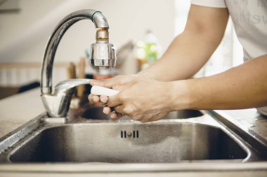 Koronavirüsün yayılmasını önlemek için her zaman temiz ellerle başlayın (Covid-19). Asyalı bir adamın evde ellerini yıkarken çekilmiş görüntüsü.