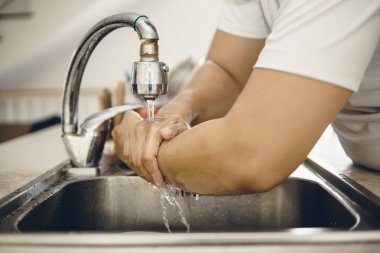 Koronavirüsün yayılmasını önlemek için her zaman temiz ellerle başlayın (Covid-19). Asyalı bir adamın evde ellerini yıkarken çekilmiş görüntüsü.