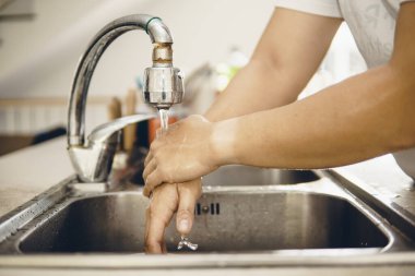 Koronavirüsün yayılmasını önlemek için her zaman temiz ellerle başlayın (Covid-19). Asyalı bir adamın evde ellerini yıkarken çekilmiş görüntüsü.