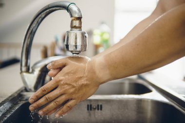 Koronavirüsün yayılmasını önlemek için her zaman temiz ellerle başlayın (Covid-19). Asyalı bir adamın evde ellerini yıkarken çekilmiş görüntüsü.