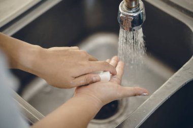 Koronavirüsün yayılmasını önlemek için her zaman temiz ellerle başlayın (Covid-19). Asyalı bir adamın evde ellerini yıkarken çekilmiş görüntüsü.