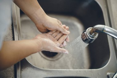 Koronavirüsün yayılmasını önlemek için her zaman temiz ellerle başlayın (Covid-19). Asyalı bir adamın evde ellerini yıkarken çekilmiş görüntüsü.