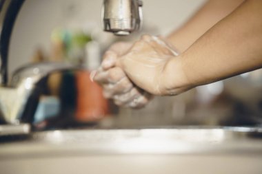 Koronavirüsün yayılmasını önlemek için her zaman temiz ellerle başlayın (Covid-19). Asyalı bir adamın evde ellerini yıkarken çekilmiş görüntüsü.