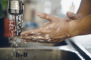 Koronavirüsün yayılmasını önlemek için her zaman temiz ellerle başlayın (Covid-19). Asyalı bir adamın evde ellerini yıkarken çekilmiş görüntüsü.