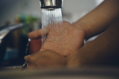 Koronavirüsün yayılmasını önlemek için her zaman temiz ellerle başlayın (Covid-19). Asyalı bir adamın evde ellerini yıkarken çekilmiş görüntüsü.