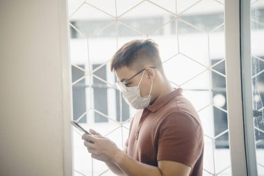 Yeni Coronavirus Covid-19 zatürree salgını sırasında beyaz cerrahi maske takan ve cep telefonu kullanan genç bir Asyalı 'ya yaklaş.