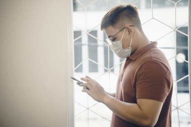 Yeni Coronavirus Covid-19 zatürree salgını sırasında beyaz cerrahi maske takan ve cep telefonu kullanan genç bir Asyalı 'ya yaklaş.