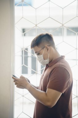 Yeni Coronavirus Covid-19 zatürree salgını sırasında beyaz cerrahi maske takan ve cep telefonu kullanan genç bir Asyalı 'ya yaklaş.