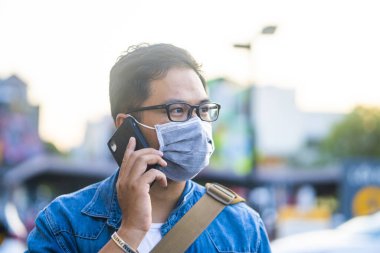 Sokakta telefon kullanırken ameliyat maskesi takan bir adam. Mikropları, zehirli dumanları ve tozu önlemek için koruyucu maske takan genç bir adamın portresi. Bakteriyel enfeksiyonun önlenmesi Corona virüsü veya Covid 19 sokaklarda ve bahçelerde.