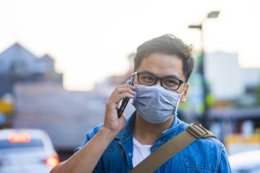 Sokakta telefon kullanırken ameliyat maskesi takan bir adam. Mikropları, zehirli dumanları ve tozu önlemek için koruyucu maske takan genç bir adamın portresi. Bakteriyel enfeksiyonun önlenmesi Corona virüsü veya Covid 19 sokaklarda ve bahçelerde.
