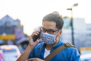 Sokakta telefon kullanırken ameliyat maskesi takan bir adam. Mikropları, zehirli dumanları ve tozu önlemek için koruyucu maske takan genç bir adamın portresi. Bakteriyel enfeksiyonun önlenmesi Corona virüsü veya Covid 19 sokaklarda ve bahçelerde.