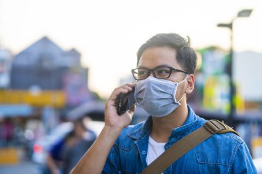 Sokakta telefon kullanırken ameliyat maskesi takan bir adam. Mikropları, zehirli dumanları ve tozu önlemek için koruyucu maske takan genç bir adamın portresi. Bakteriyel enfeksiyonun önlenmesi Corona virüsü veya Covid 19 sokaklarda ve bahçelerde.