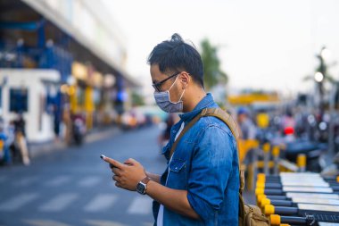 Sokakta telefon kullanırken ameliyat maskesi takan bir adam. Mikropları, zehirli dumanları ve tozu önlemek için koruyucu maske takan genç bir adamın portresi. Bakteriyel enfeksiyonun önlenmesi Corona virüsü veya Covid 19 sokaklarda ve bahçelerde.