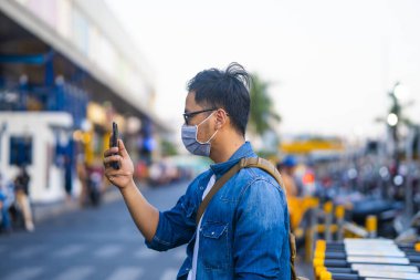 Sokakta telefon kullanırken ameliyat maskesi takan bir adam. Mikropları, zehirli dumanları ve tozu önlemek için koruyucu maske takan genç bir adamın portresi. Bakteriyel enfeksiyonun önlenmesi Corona virüsü veya Covid 19 sokaklarda ve bahçelerde.