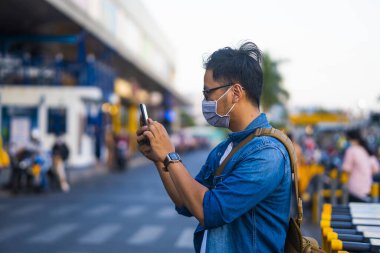 Sokakta telefon kullanırken ameliyat maskesi takan bir adam. Mikropları, zehirli dumanları ve tozu önlemek için koruyucu maske takan genç bir adamın portresi. Bakteriyel enfeksiyonun önlenmesi Corona virüsü veya Covid 19 sokaklarda ve bahçelerde.