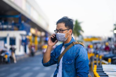 Sokakta telefon kullanırken ameliyat maskesi takan bir adam. Mikropları, zehirli dumanları ve tozu önlemek için koruyucu maske takan genç bir adamın portresi. Bakteriyel enfeksiyonun önlenmesi Corona virüsü veya Covid 19 sokaklarda ve bahçelerde.