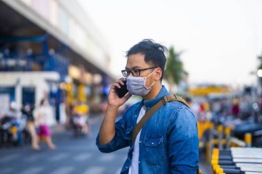 Sokakta telefon kullanırken ameliyat maskesi takan bir adam. Mikropları, zehirli dumanları ve tozu önlemek için koruyucu maske takan genç bir adamın portresi. Bakteriyel enfeksiyonun önlenmesi Corona virüsü veya Covid 19 sokaklarda ve bahçelerde.