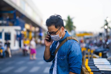 Sokakta telefon kullanırken ameliyat maskesi takan bir adam. Mikropları, zehirli dumanları ve tozu önlemek için koruyucu maske takan genç bir adamın portresi. Bakteriyel enfeksiyonun önlenmesi Corona virüsü veya Covid 19 sokaklarda ve bahçelerde.